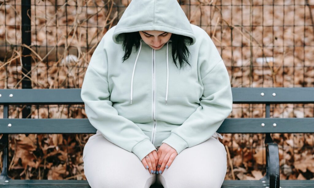 A sad woman sitting on a bench looking down