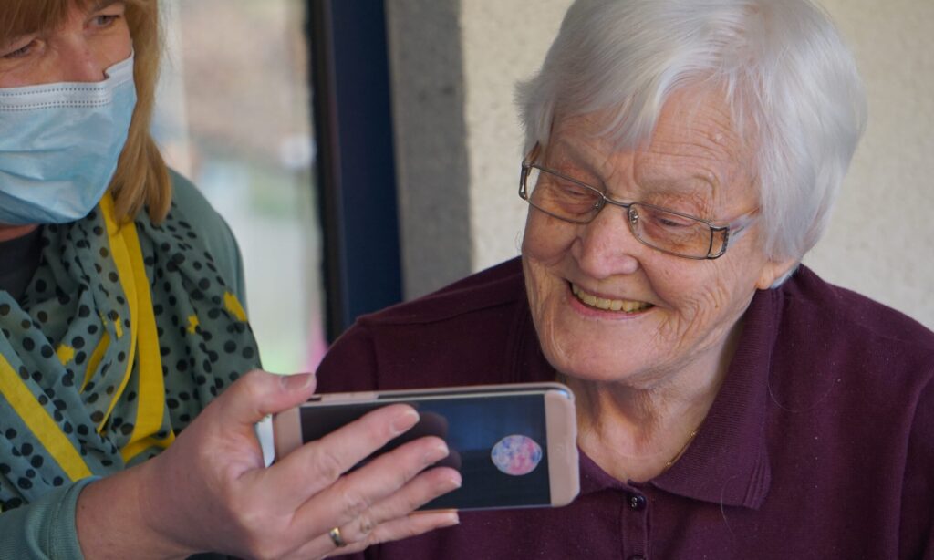 A woman viewing a phone with her carer